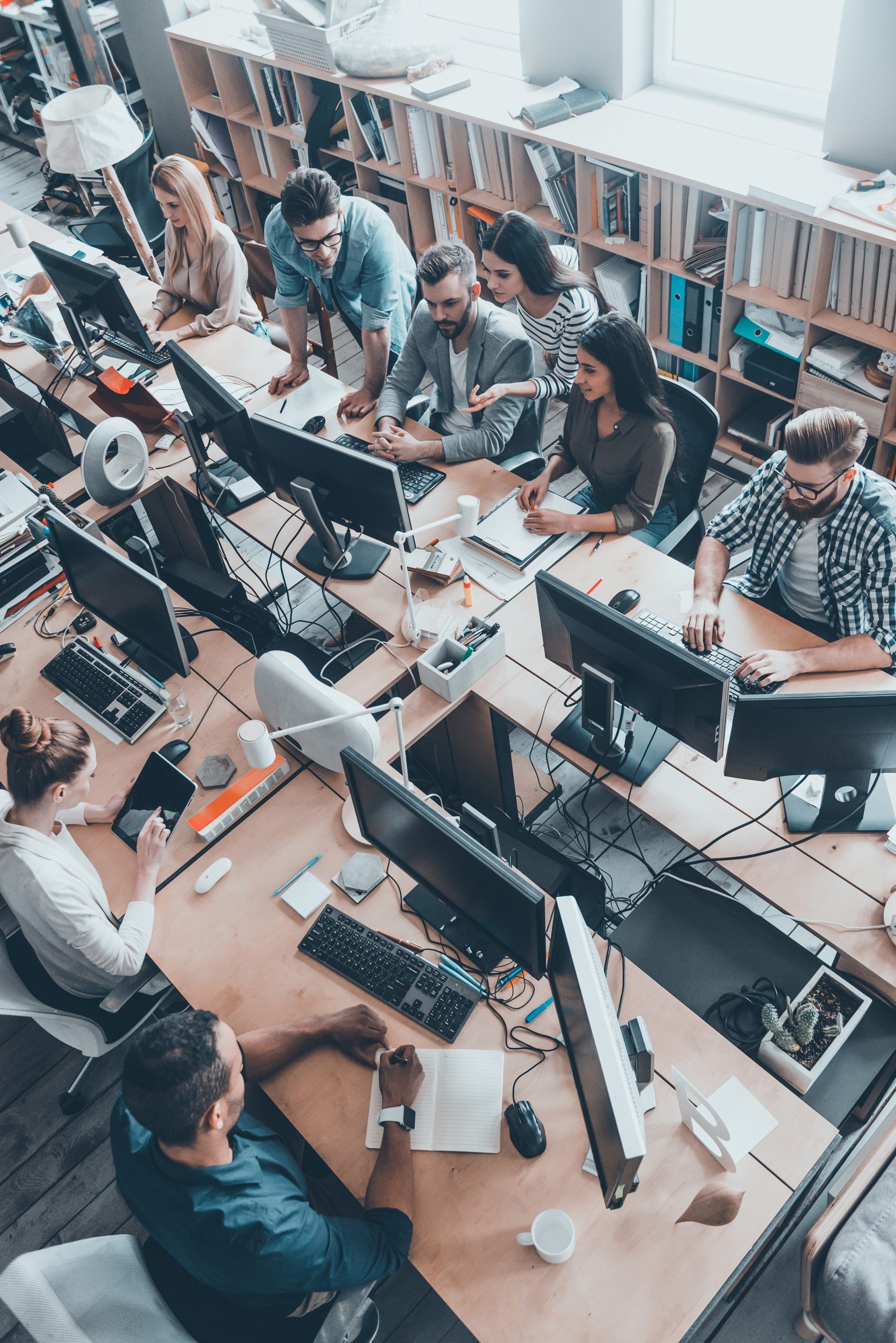 Successful team. Top view of group of young business people in smart casual wear working together while sitting at the large office desk